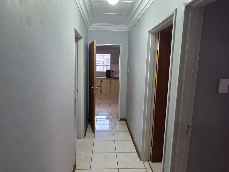 A functional hallway with tiled flooring and neutral wall finishes, providing access to multiple rooms and a view through to the kitchen area.