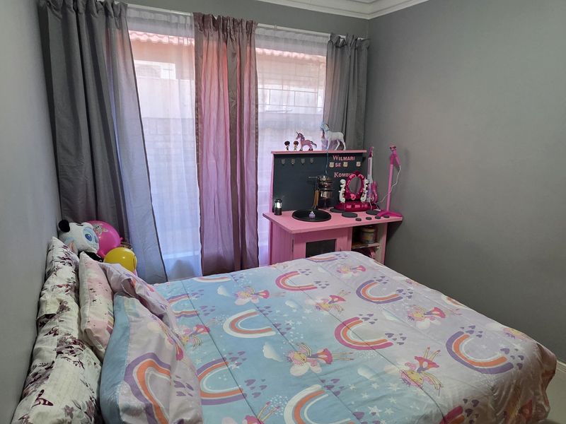 A standard bedroom featuring neutral grey walls, a wall-mounted panel heater, and large windows with curtain tracks.