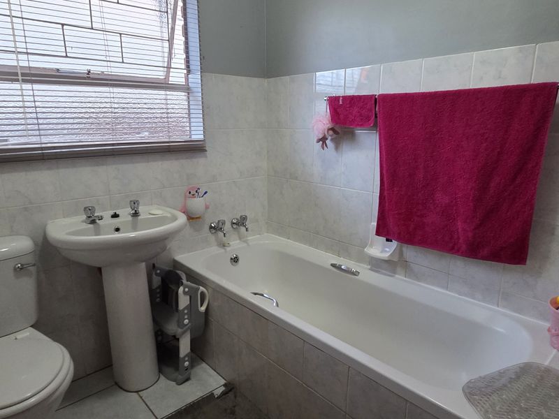 A functional bathroom featuring a pedestal basin, bathtub, and toilet with neutral wall tiling and natural light from a window.