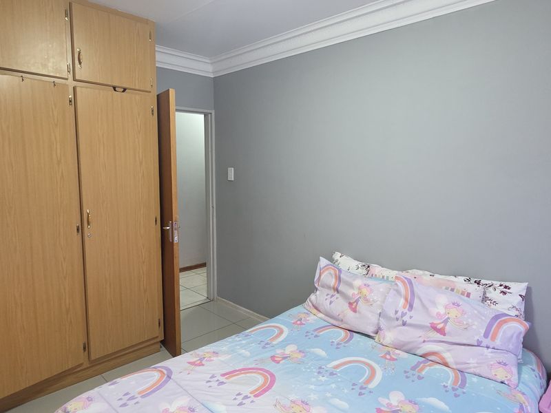 A bedroom featuring built-in wooden cupboards, tiled flooring, and decorative ceiling cornices.