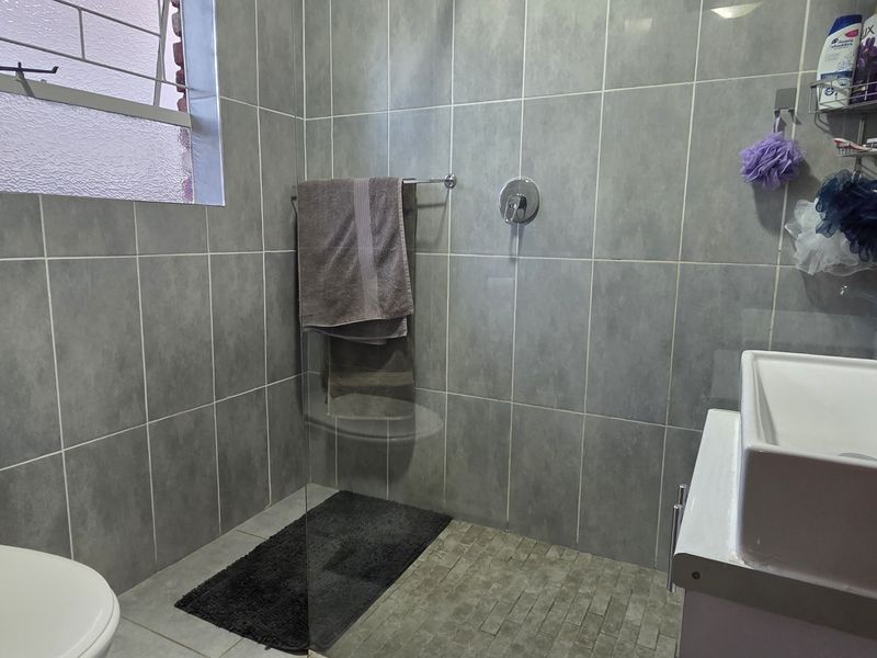 A modern bathroom featuring grey wall tiles, a glass-enclosed shower, a contemporary basin with vanity, and a toilet.