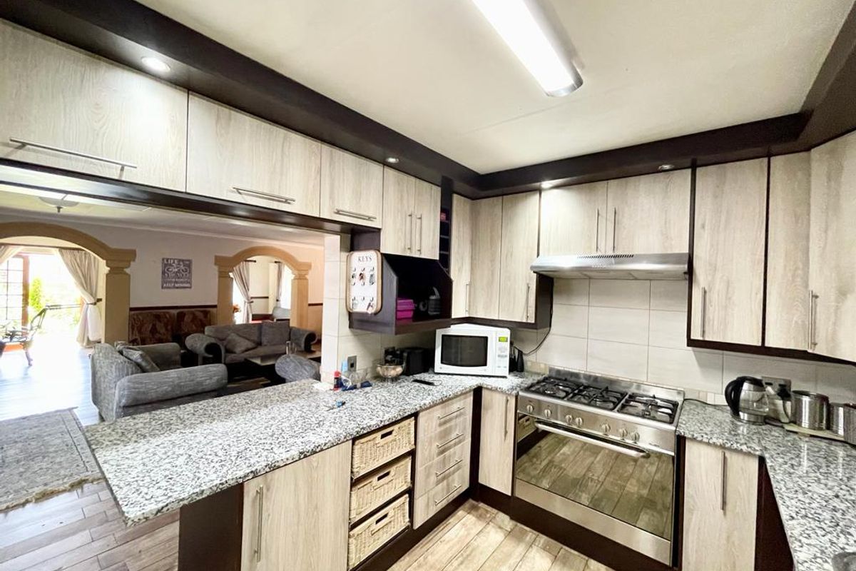 A functional kitchen featuring light wood-grain cabinetry, granite countertops, a built-in gas hob, and an extractor fan, overlooking an adjacent living area.