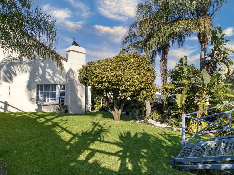A well-maintained rear garden featuring a lush lawn, mature trees, and an external metal staircase leading to the upper level of the townhouse.