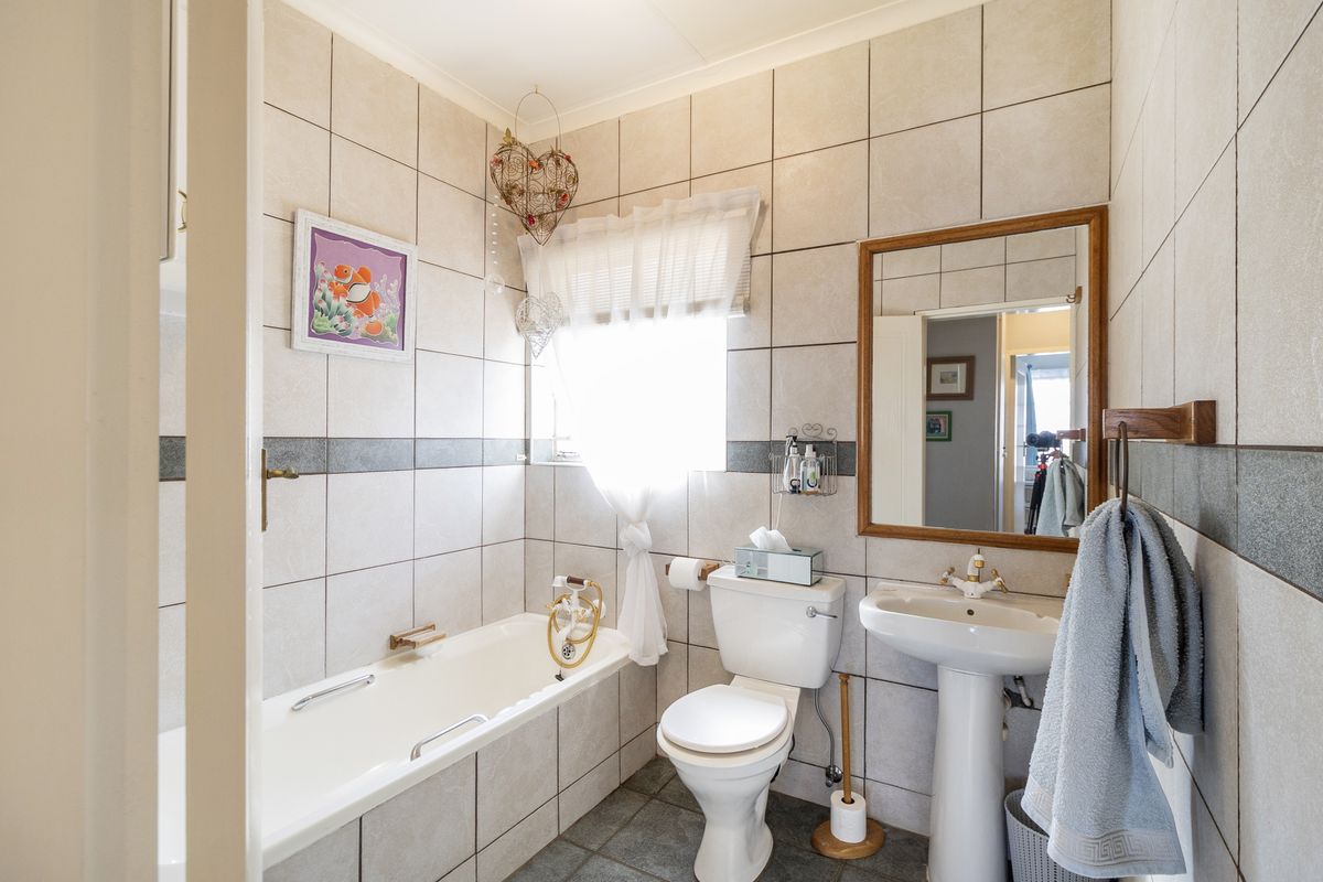 A functional bathroom featuring a bathtub, pedestal basin, and toilet with neutral wall and floor tiling.