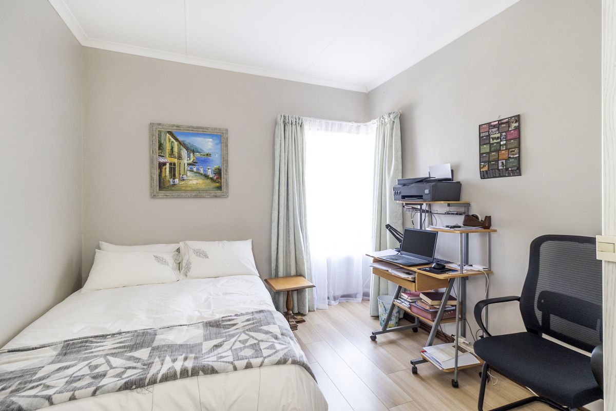 A well-maintained bedroom featuring light-toned laminate flooring, neutral wall finishes, and a window with installed curtain tracks.