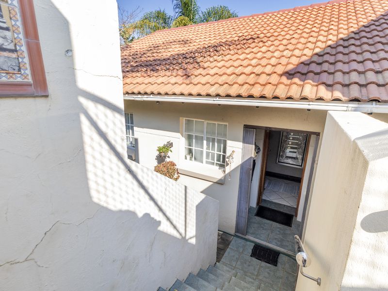 Rear exterior view of the townhouse featuring a tiled staircase leading to the entrance, terracotta roof tiles, and visible exterior wall plastering.