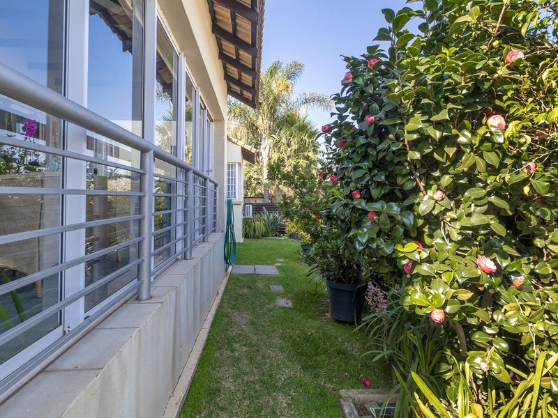 A well-maintained rear garden area featuring a manicured lawn, established flowering shrubs, and a paved patio edge with modern aluminium sliding doors.