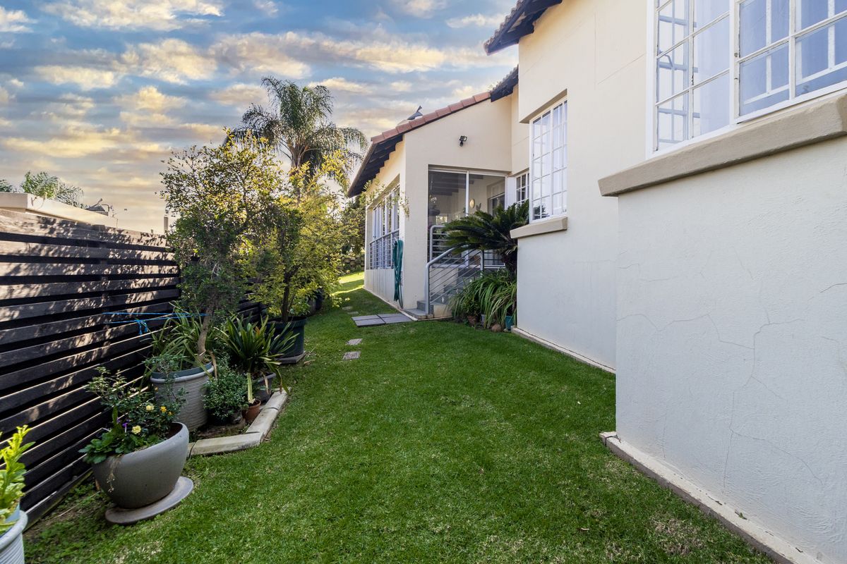 A view of the rear garden featuring a well-maintained lawn, timber fencing, and access to the side of the townhouse.