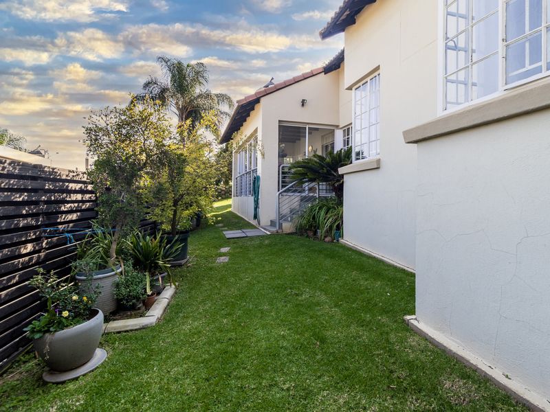 A view of the rear garden featuring a well-maintained lawn, timber fencing, and access to the side of the townhouse.