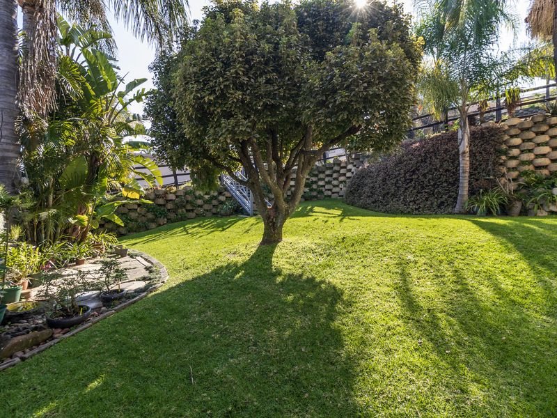 A well-maintained private garden featuring a lush green lawn, mature trees, and tiered stone retaining walls.