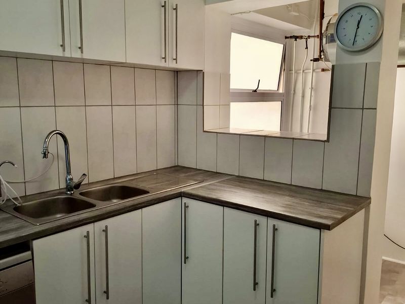 A functional kitchen featuring white cabinetry, laminate countertops, a stainless steel double sink, and a convenient pass-through window to the adjacent living area.