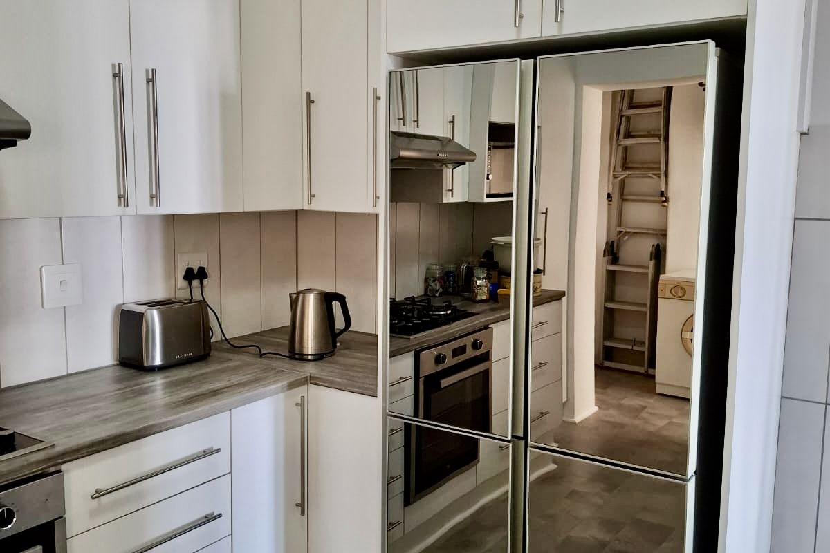 Modern kitchen featuring white cabinetry, laminate countertops, built-in oven, gas hob, and extractor fan, with a view into the adjacent laundry area.