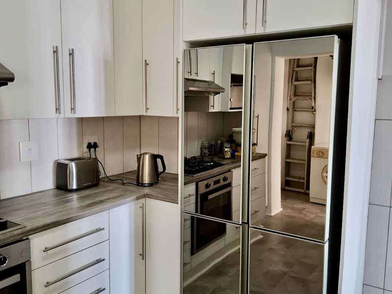 Modern kitchen featuring white cabinetry, laminate countertops, built-in oven, gas hob, and extractor fan, with a view into the adjacent laundry area.