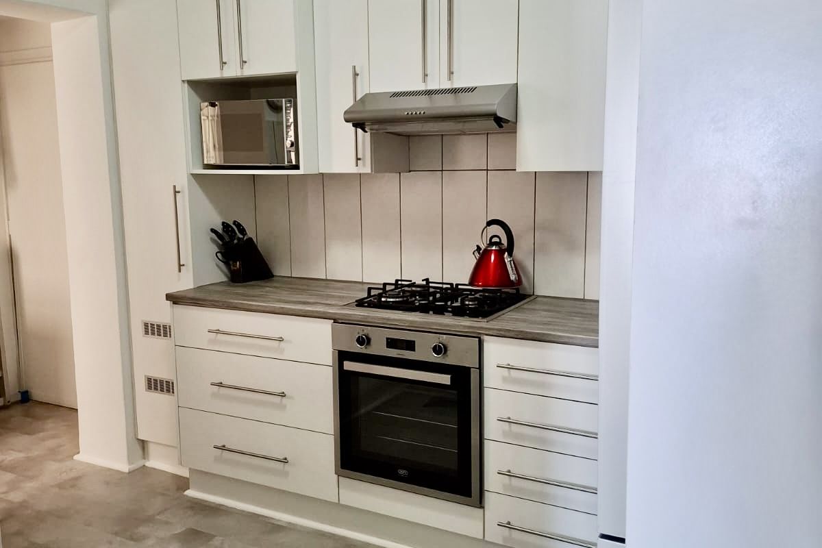 Modern kitchen featuring white cabinetry, laminate countertops, gas hob, built-in oven, extractor fan, and tiled backsplash with durable vinyl flooring.