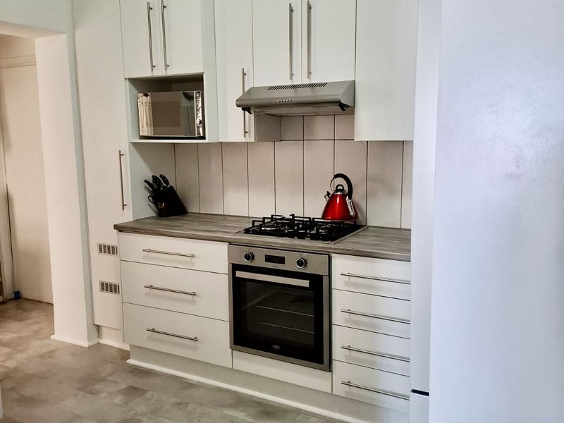 Modern kitchen featuring white cabinetry, laminate countertops, gas hob, built-in oven, extractor fan, and tiled backsplash with durable vinyl flooring.