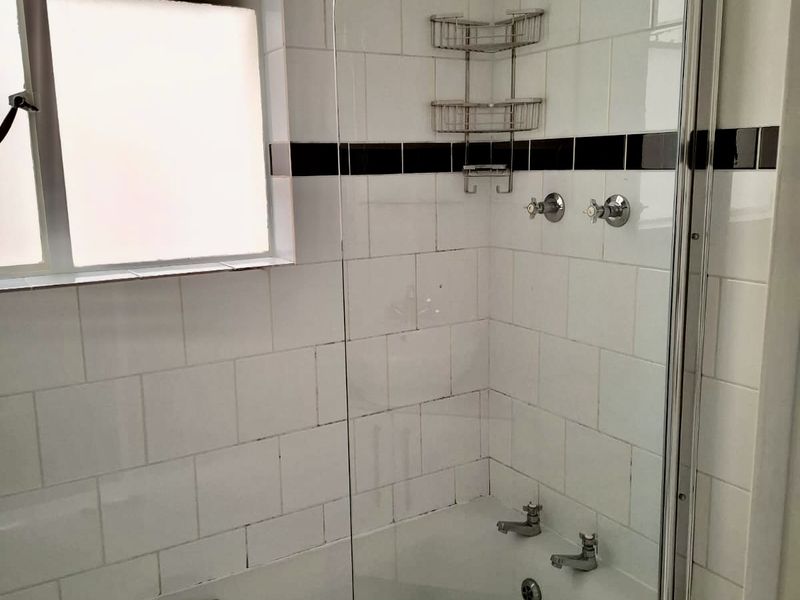 A functional bathroom featuring a bathtub with a shower head, glass screen, and classic white wall tiling with a black accent border.