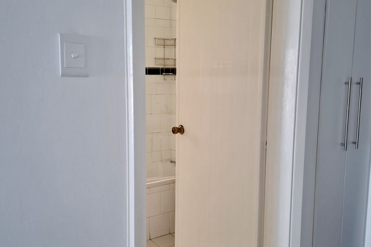 A view through a doorway into a bathroom featuring tiled flooring, a bathtub, and shower area, adjacent to built-in storage cupboards.