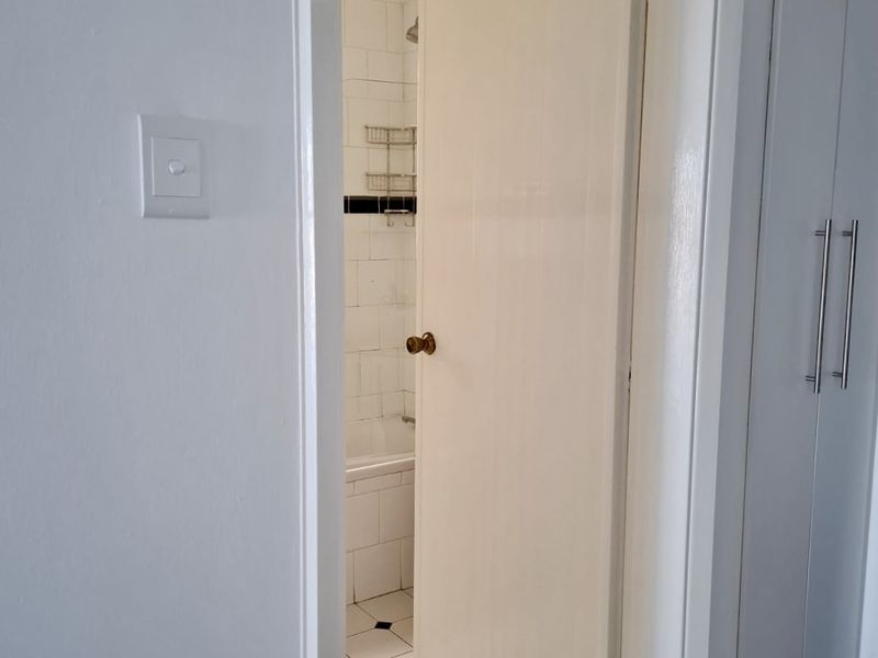 A view through a doorway into a bathroom featuring tiled flooring, a bathtub, and shower area, adjacent to built-in storage cupboards.