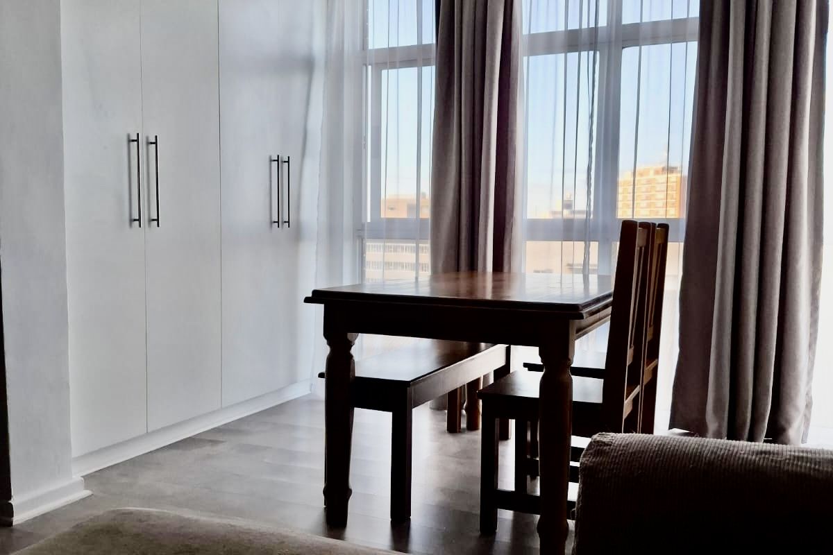 A bright bedroom featuring floor-to-ceiling built-in cupboards, large windows allowing ample natural light, and modern laminate flooring.