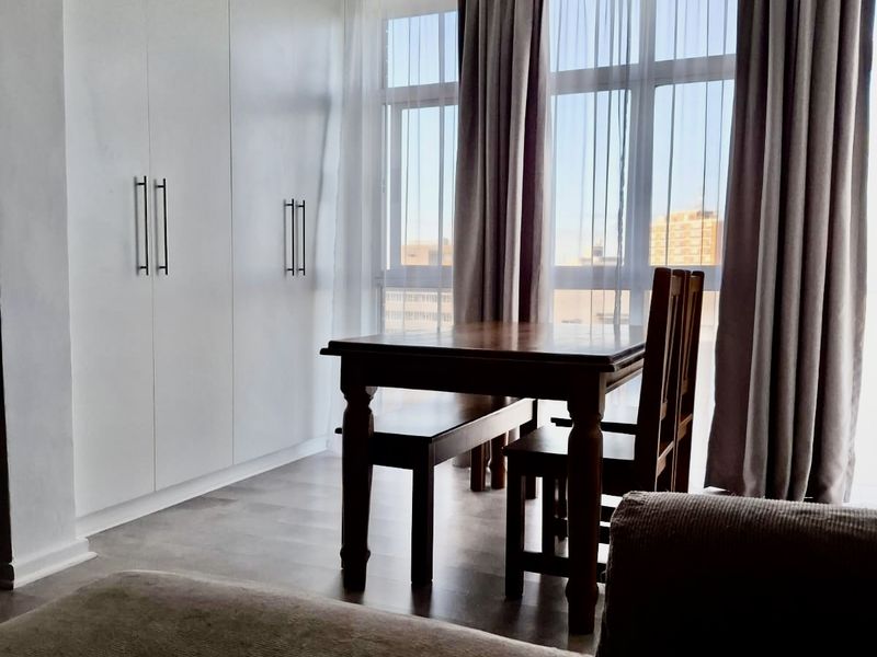 A bright bedroom featuring floor-to-ceiling built-in cupboards, large windows allowing ample natural light, and modern laminate flooring.