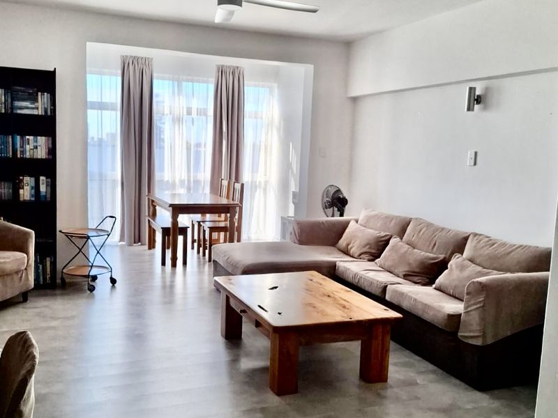 Spacious open-plan living and dining area featuring modern laminate flooring, a ceiling fan, and large windows allowing for ample natural light.