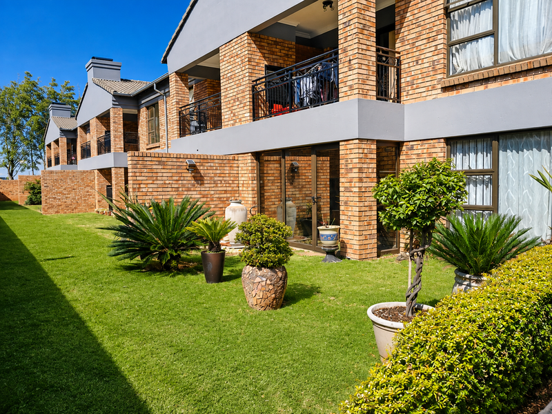 Rear view of a modern face brick apartment complex featuring private balconies, sliding glass doors, and a well-maintained communal garden area.