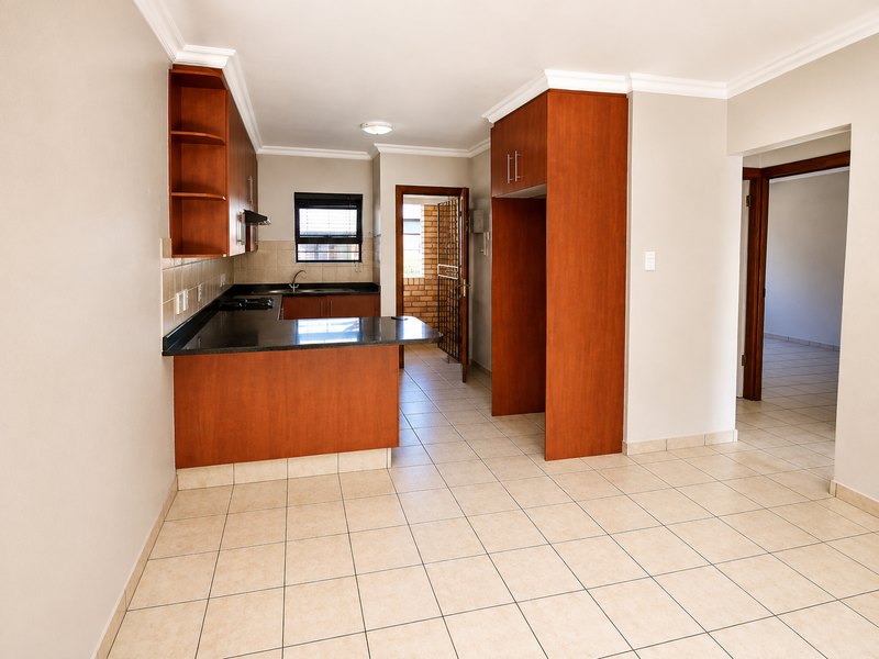 A clean, functional kitchen featuring warm-toned cabinetry, granite countertops, and tiled flooring, with an open-plan layout leading to adjacent living spaces.