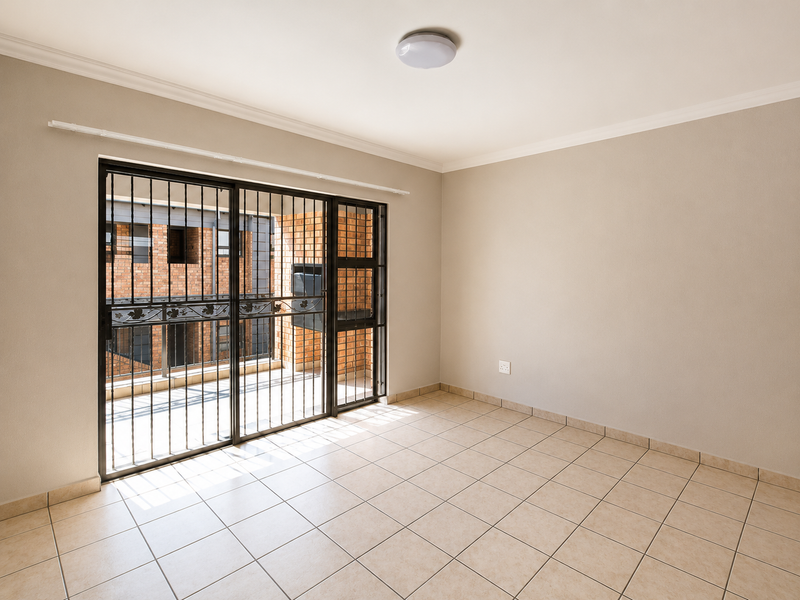 A bright, empty living room featuring neutral tiled flooring, coving, and a large sliding glass door with an integrated security gate leading to a balcony.