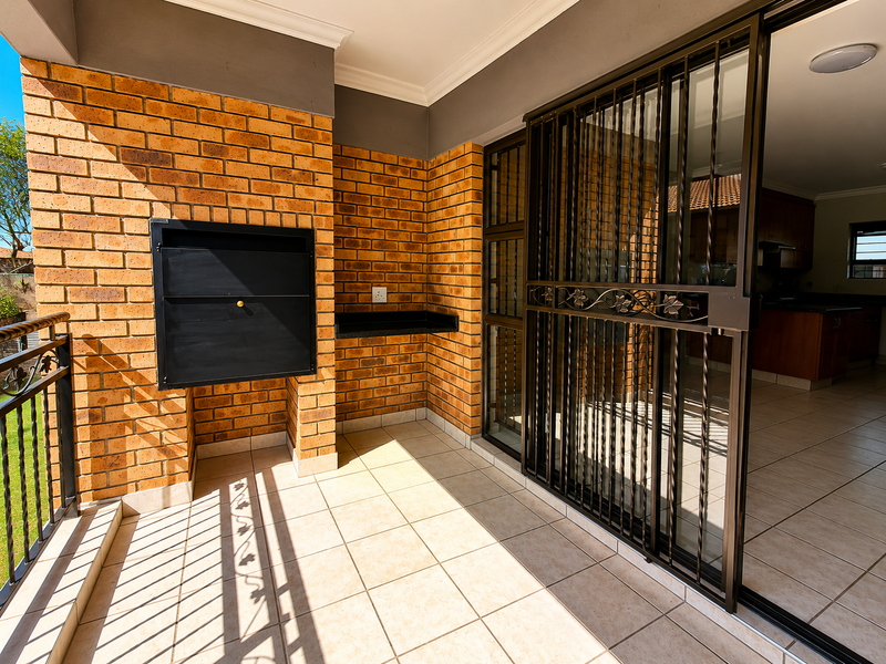 A covered balcony featuring a built-in braai, granite prep surface, tiled flooring, and a secure sliding gate leading into the apartment interior.