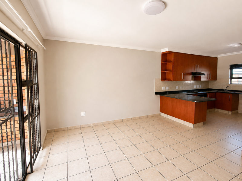 Spacious open-plan living area featuring tiled floors and a functional kitchen with granite countertops and built-in cabinetry, leading to an outdoor area.