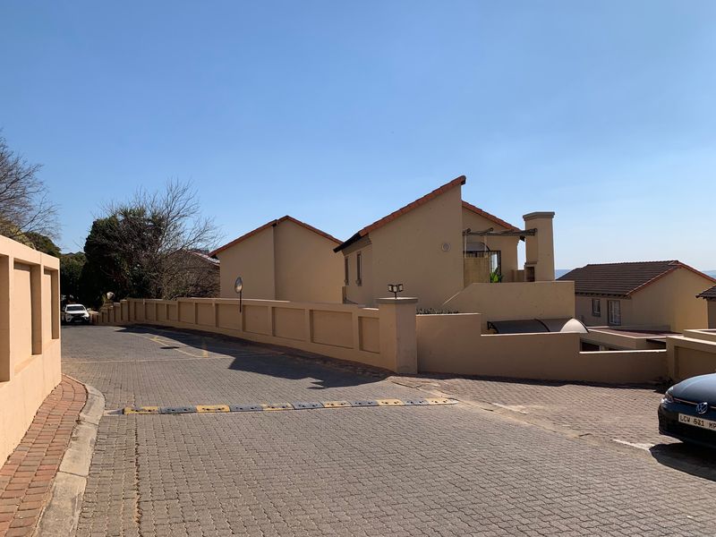 A view of the townhouse complex entrance featuring paved driveways, perimeter walling, and established residential architecture under a clear sky.