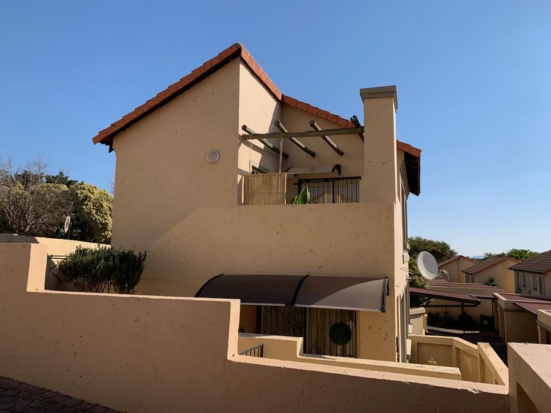 Rear view of a townhouse featuring a balcony with a timber pergola, terracotta roof tiles, and a private boundary wall.