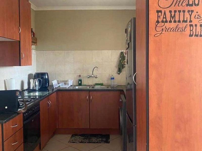 A functional kitchen featuring wood-finish cabinetry, laminate countertops, a double basin sink, and built-in cooking appliances with tiled flooring.