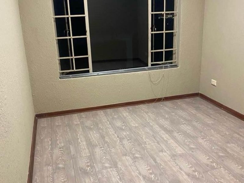 An empty bedroom featuring wood-look laminate flooring, neutral walls, and a window fitted with security burglar bars.