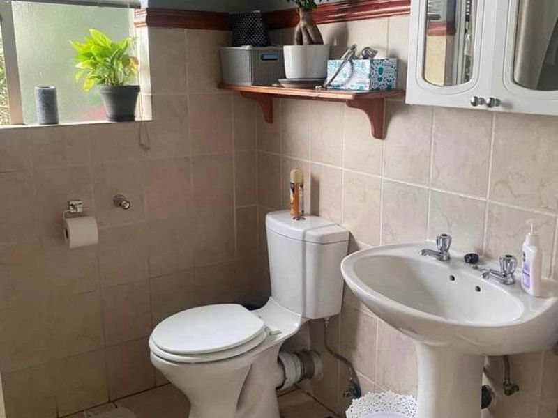 A functional bathroom featuring a pedestal basin, toilet, and tiled finishes, offering a practical layout with potential for modern cosmetic updates.