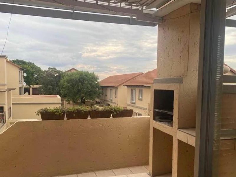 Covered balcony featuring a built-in braai and tiled flooring, offering an outdoor entertainment space with views of the surrounding townhouse complex.