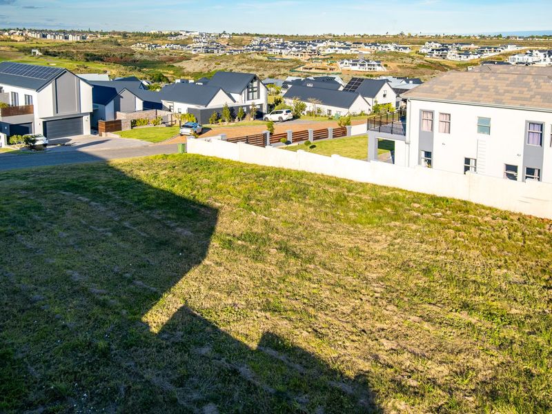 An elevated view of a vacant residential plot situated within a developed estate, featuring surrounding homes and clear boundary lines.