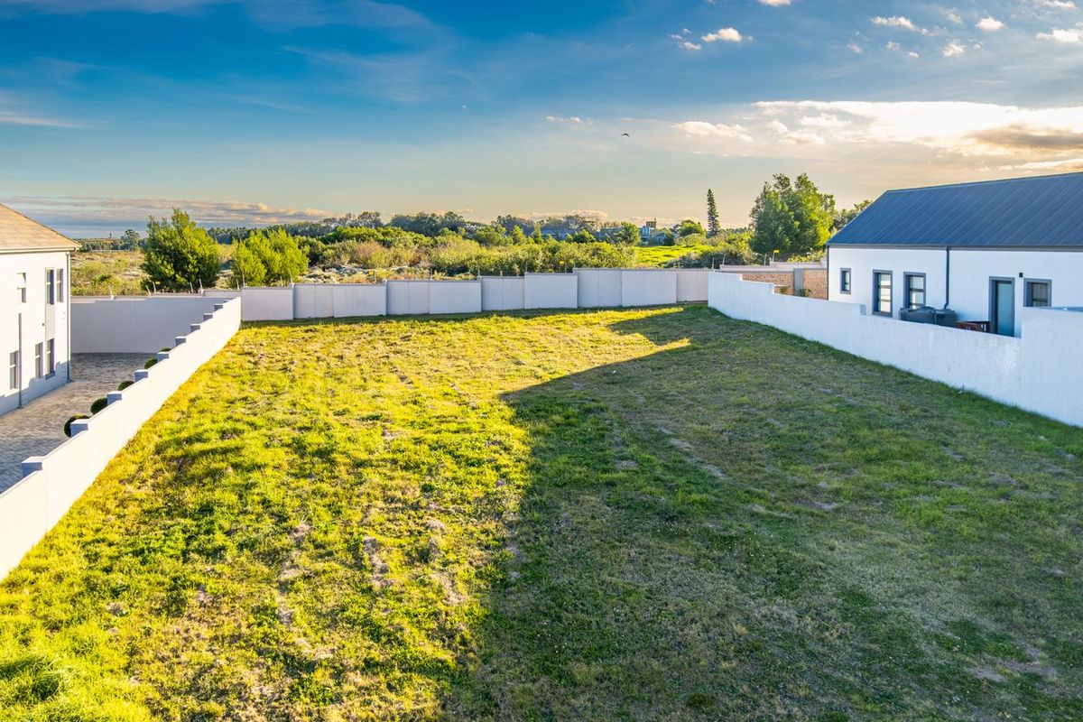 A spacious vacant residential plot featuring a well-maintained grass lawn, enclosed by perimeter boundary walls, situated between existing residential structures.