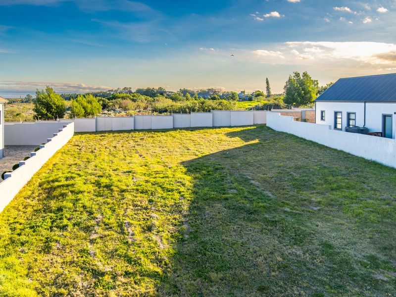 A spacious vacant residential plot featuring a well-maintained grass lawn, enclosed by perimeter boundary walls, situated between existing residential structures.