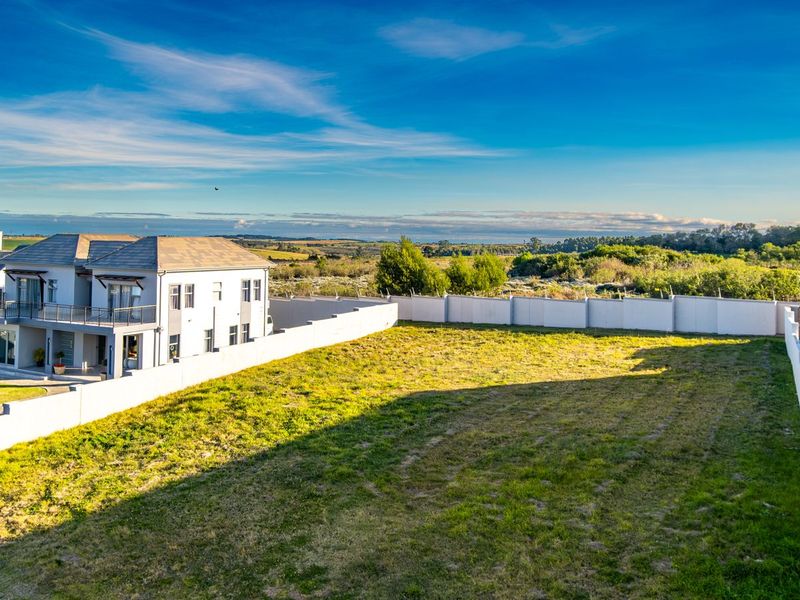 Aerial view of a vacant residential plot featuring a perimeter wall with electric fencing and established lawn, adjacent to existing residential properties.