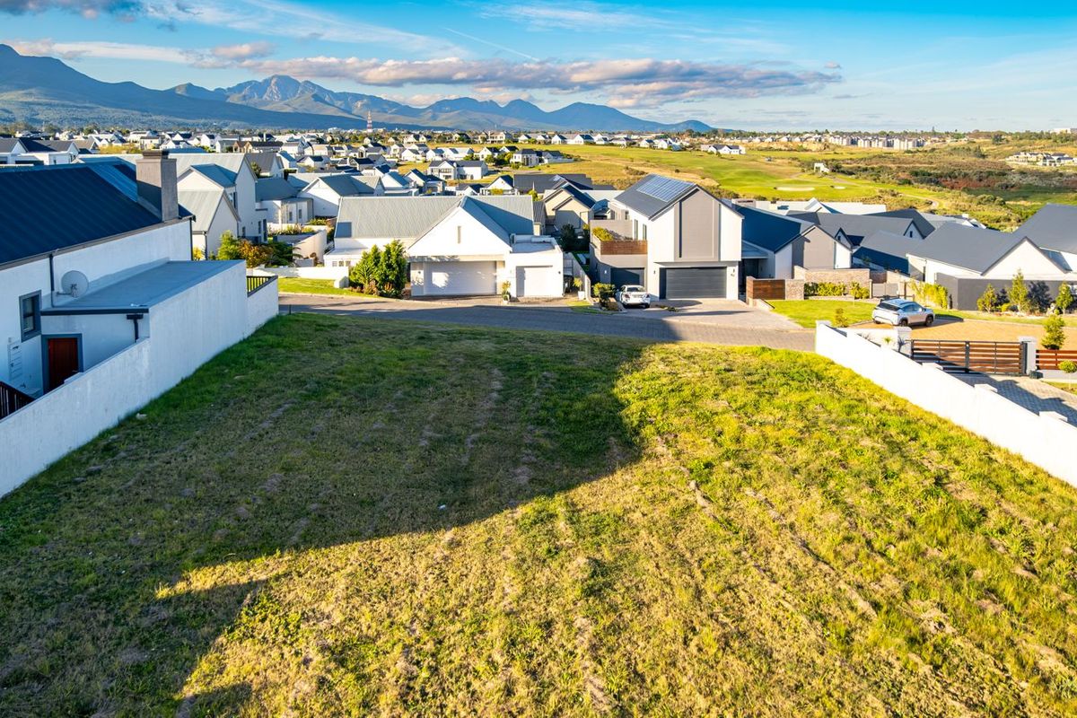 An elevated aerial view of a vacant residential plot situated within a developed estate, featuring surrounding homes and mountain views.