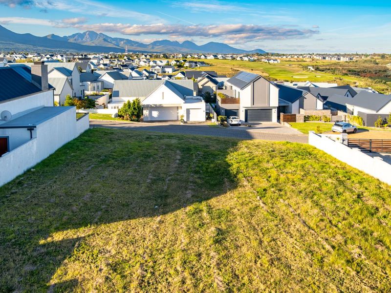 An elevated aerial view of a vacant residential plot situated within a developed estate, featuring surrounding homes and mountain views.
