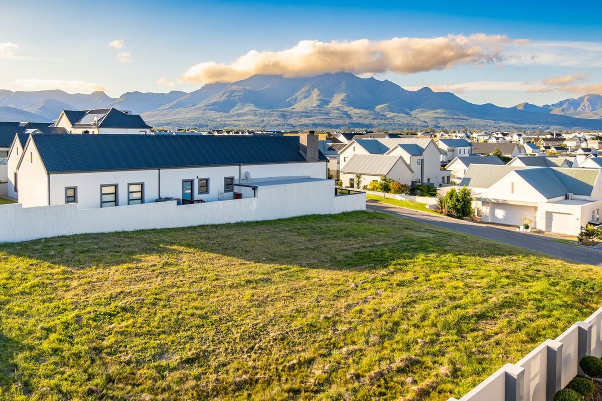 An elevated view of a vacant residential plot in a developed estate, featuring mountain views and surrounding modern residential properties.