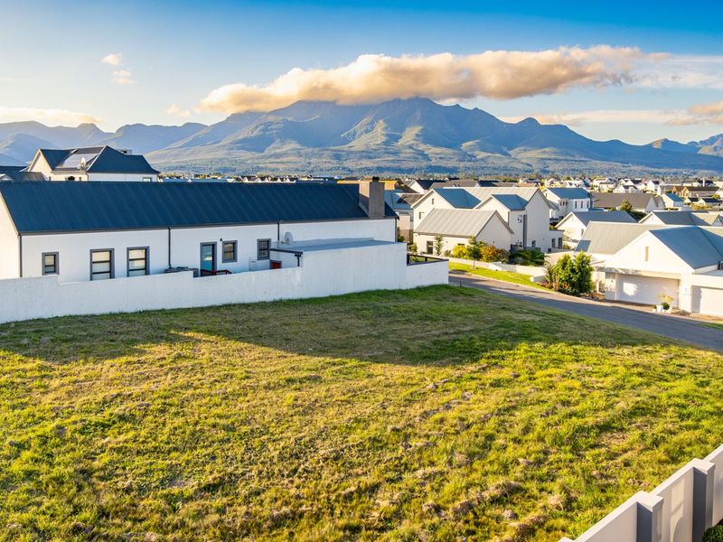 An elevated view of a vacant residential plot in a developed estate, featuring mountain views and surrounding modern residential properties.