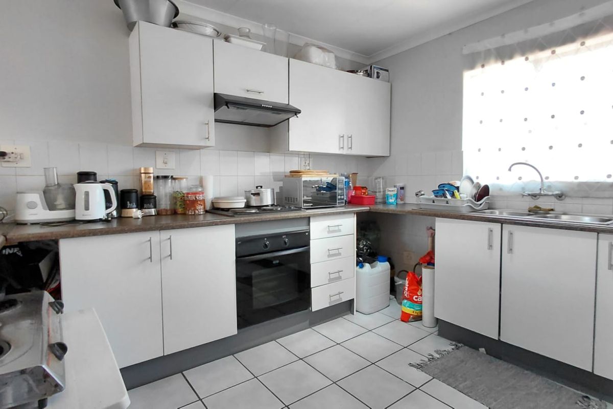 Functional kitchen featuring white cabinetry, laminate countertops, built-in oven, extractor fan, and tiled flooring with a practical layout.