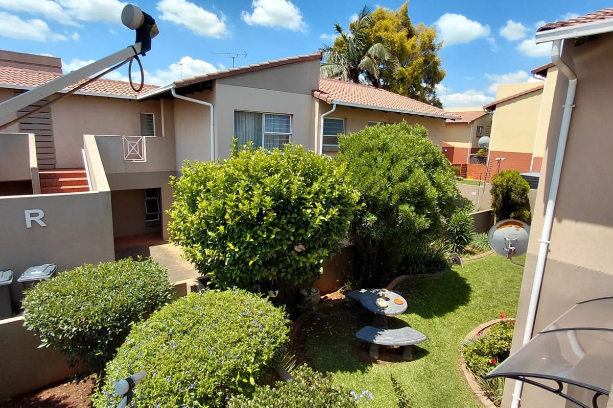 A view of the rear exterior of the apartment complex, featuring a well-maintained garden, tiled roofing, and paved access paths.
