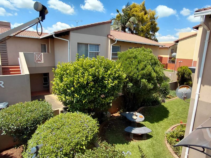 A view of the rear exterior of the apartment complex, featuring a well-maintained garden, tiled roofing, and paved access paths.