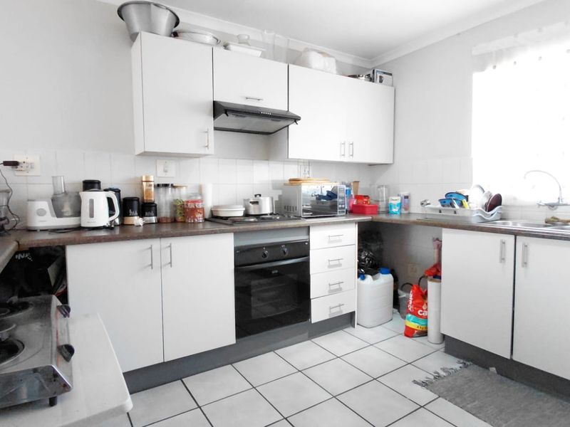 A functional kitchen featuring white cabinetry, laminate countertops, a built-in oven with extractor fan, and tiled flooring with a tiled backsplash.