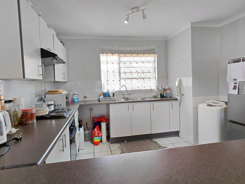 Functional kitchen featuring white cabinetry, laminate countertops, tiled backsplash, and ceramic flooring, providing a practical workspace with integrated cooking and cleaning facilities.