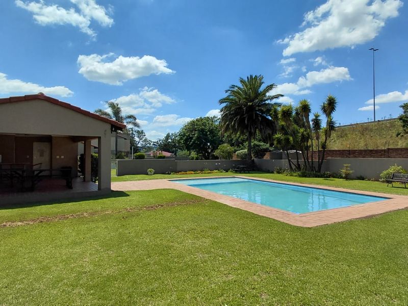 Outdoor pool area featuring a swimming pool with brick coping, a spacious lawn, and an adjacent covered patio structure.
